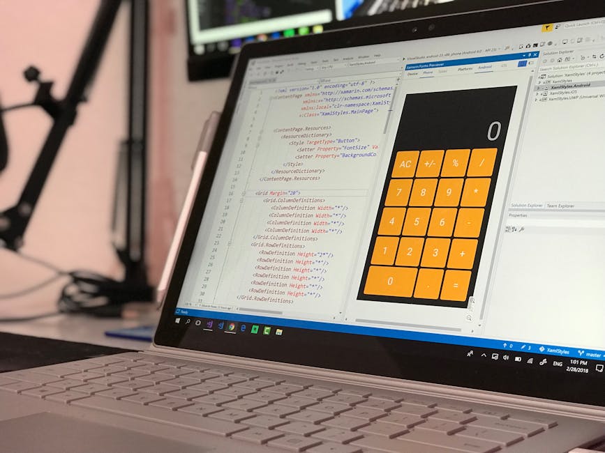 A close-up view of a person's hand using a laptop with a silver metallic finish on a wooden surface. The laptop screen displays lines of programming code with syntax highlighting, including various te